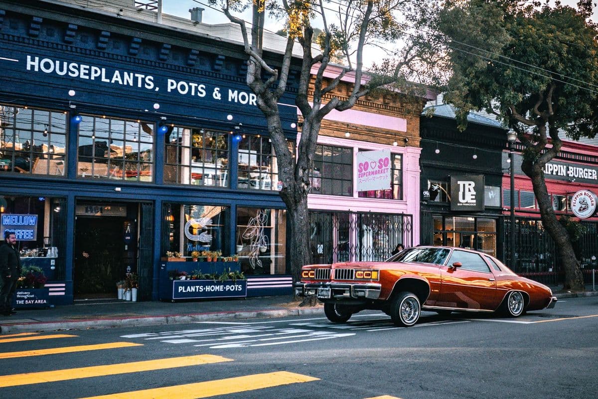 A vintage lowrider car parked in front of colorful shops in San Francisco, California.
